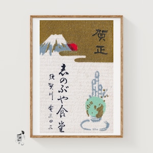 Könnte beinhalten: Ein gerahmter Druck mit texturiertem weißem Hintergrund, einem goldenen oberen Bereich, einem schneebedeckten Berg, einer roten Sonne und japanischer Kalligrafie. Das Design enthält ein grünes, globusartiges Element mit Goldakzenten und schwarzem Text.