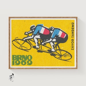 Puede incluir: Impresión artística vintage en caja de cerillas que representa a dos ciclistas en bicicleta tándem. Los ciclistas visten camisetas azules y blancas con detalles rojos. El fondo es amarillo y el texto "BRNO 1969" es verde. También está el texto "ZÁVOD TANDEMŮ".
