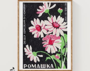 May include: A framed vintage matchbox label print featuring white and pink daisy flowers against a black background. The text includes the Cyrillic word ROMASHKA, meaning chamomile, along with technical production details in Russian text.