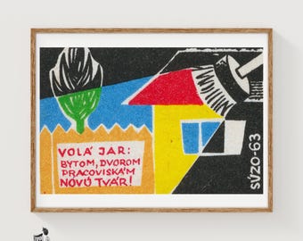 May include: A framed print featuring a stylized graphic illustration with a red roof, yellow house, blue sky, and green tree. The text reads: VOLA JAR: BYTOM, DVOROM PRACOVISKÁM NOVÚ TVÁR! and SVZO-63. The artwork uses bold colors and geometric shapes.