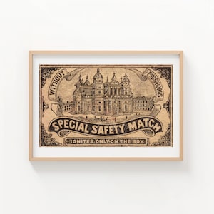 May include: A framed print of a vintage matchbox label. The label features an illustration of a grand building with multiple domes and towers. The text reads "SPECIAL SAFETY MATCH" and "IGNITES ONLY ON THE BOX". The frame is a light wood color.
