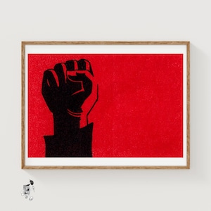 May include: A rectangular framed print featuring a bold black silhouette of a raised fist against a vibrant, textured red background. The artwork is enclosed in a light brown wooden frame, presenting a high-contrast graphic design.