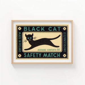 May include: Framed print of a vintage matchbox label. The label features a black cat silhouette with blue eyes, the text "BLACK CAT SAFETY MATCH", and "AVERAGE CONTENTS 50". The label is set against a cream background.