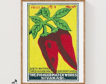 May include: A framed vintage matchbox label print featuring a bright yellow background with a central illustration of two red chili peppers and green leaves. The text reads PRICE RE 0-0-9, DISTRIBUTORS THE SIVAKASI MATCHES EXPORTING CO, THE PIONEER MATCH WORKS SIVAKASI.