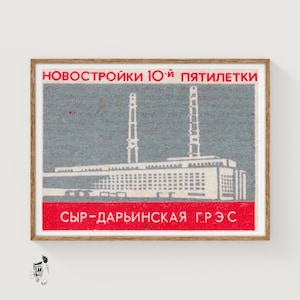 Può includere: Etichetta vintage di scatola di fiammiferi con un'illustrazione di una centrale elettrica. Il design include un grande edificio con due alti camini su sfondo grigio. Il testo in alto è rosso e quello in basso è bianco.