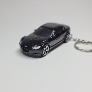 May include: A black Mazda MX-5 Miata keychain with a silver key ring. The car is a detailed replica with a black finish and silver wheels.