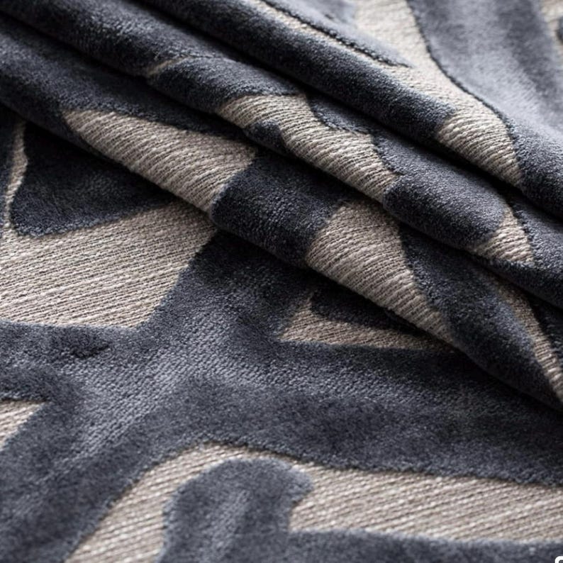 Puede incluir: Primer plano de una tela plegada con un patr&oacute;n geom&eacute;trico repetitivo. El dise&ntilde;o presenta tonos de gris y azul oscuro. La tela tiene una textura suave y aterciopelada, con pliegues y sombras que a&ntilde;aden profundidad al dise&ntilde;o.