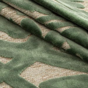 Puede incluir: Primer plano de una tela texturizada con un patr&oacute;n repetitivo. El dise&ntilde;o presenta un patr&oacute;n geom&eacute;trico en relieve verde claro sobre un fondo beige. La tela est&aacute; doblada, mostrando profundidad y textura.