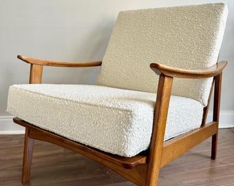 Puede incluir: Un sillón blanco con tapicería de tela texturizada y estructura de madera. El sillón tiene un respaldo y brazos curvos, y las patas son anguladas.
