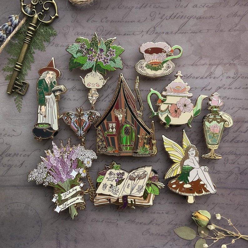 May include: A collection of ten enamel pins featuring whimsical designs, including a witch, a fairy, a teapot, a book, a house, a flower, a butterfly, and a mandrake. The pins are gold-toned and have a variety of colors.