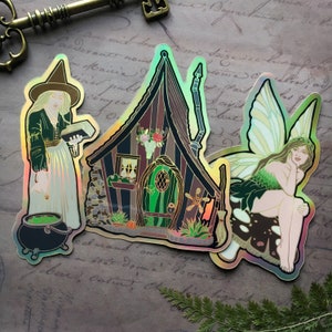 May include: Three iridescent holographic stickers featuring a witch with a cauldron, a fairy with wings, and a small cottage with a green door. The stickers are on a brown background with writing.