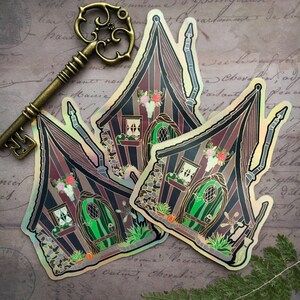 May include: Two iridescent stickers of a whimsical, striped, gothic-style house with a green door, a skull, and flowers. The stickers are on a vintage background with a gold key.