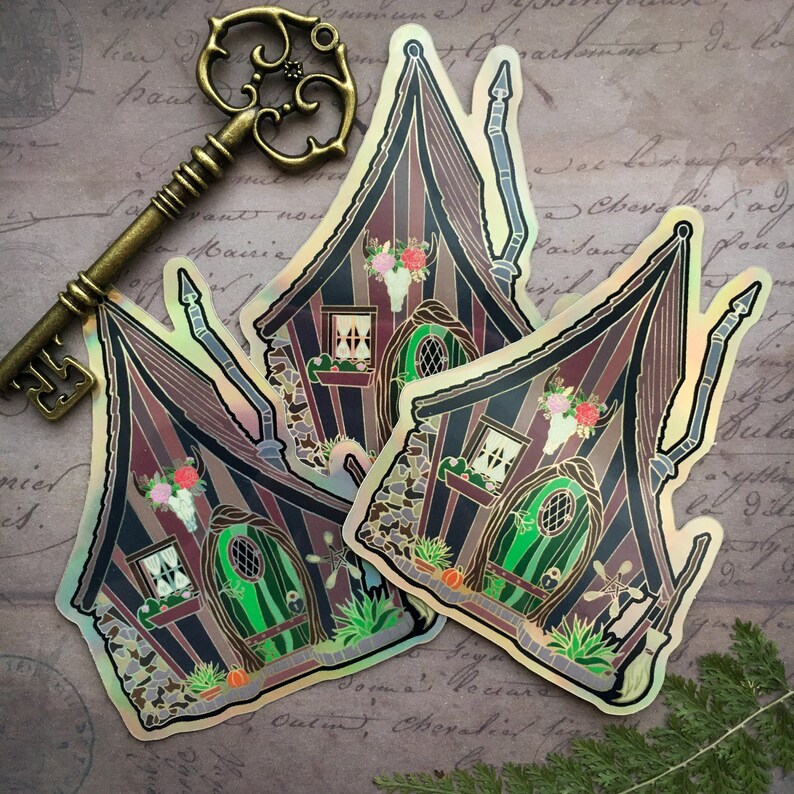 May include: Two iridescent stickers of a whimsical, striped, gothic-style house with a green door, a skull, and flowers. The stickers are on a vintage background with a gold key.