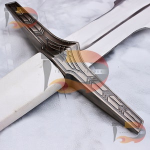 May include: Close-up of the crossguard of a sword with a silver blade and a white handle. The crossguard is made of metal and has a detailed design with geometric patterns.