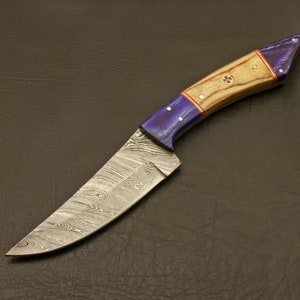 May include: A Damascus steel hunting knife with a blue and wood handle. The blade has a wavy pattern and the handle has a red accent.