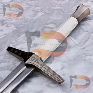 May include: A silver and white sword with a decorative handle and a black and silver cross guard. The sword has a white grip and a silver pommel. The blade is silver and has a black edge. The sword is on a white marble surface. "Terror Defender" is printed on the surface.