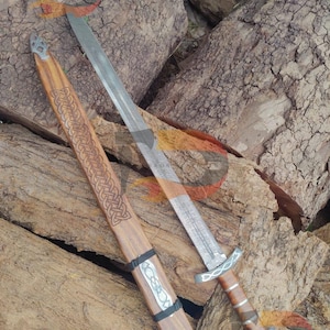 May include: A silver Viking sword with a wooden handle and a leather scabbard with intricate carvings. The scabbard is decorated with a Celtic knot design.