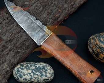 Può includere: Un coltello in acciaio Damasco con manico in legno. La lama presenta un motivo ondulato e un bordo seghettato. Il manico è marrone con un accento in ottone.