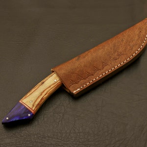 May include: A brown leather knife sheath with a decorative stitching pattern and a wooden-handled knife with a purple and wood-grain handle.