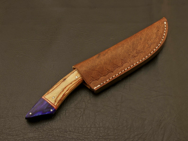May include: A brown leather knife sheath with a decorative stitching pattern and a wooden-handled knife with a purple and wood-grain handle.