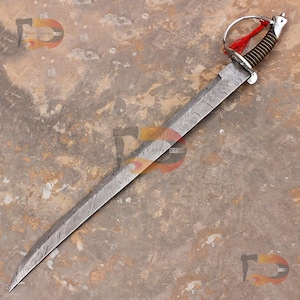 May include: A Damascus steel sword with a curved blade. The hilt features a brown and black grip, a silver guard, and a red tassel. The blade has a unique pattern, and the sword is displayed on a textured surface.