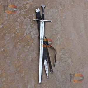 May include: A silver sword with a black leather scabbard and a silver pommel. The blade is inscribed with the text "Forged in the fires of Mount Doom, this blade is a symbol of hope and courage."