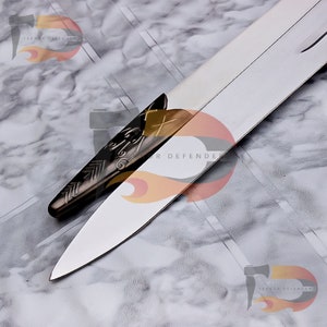 May include: Close-up of a silver and gold sword with a wolf head pommel. The sword has a sharp, pointed blade and a textured handle. The text "Terror Defender" is visible on the blade.