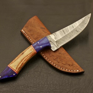 May include: A blue and brown handled knife with a Damascus steel blade, in a brown leather sheath.