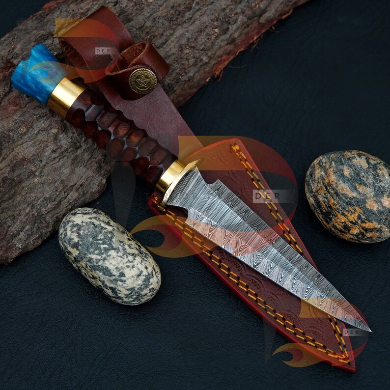 May include: A Damascus steel dagger with a blue and gold handle, in a brown leather sheath with decorative stitching.