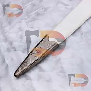 May include: Close-up of a silver sword pommel with intricate engraved designs. The pommel is pointed and has a cross-shaped design at the top.