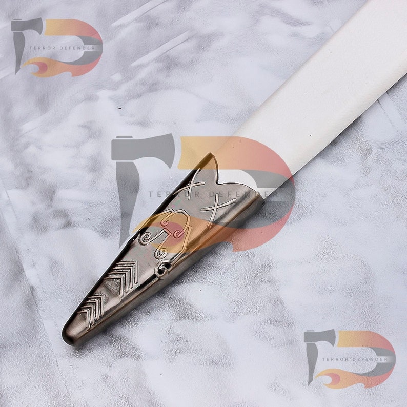 May include: Close-up of a silver sword pommel with intricate engraved designs. The pommel is pointed and has a cross-shaped design at the top.