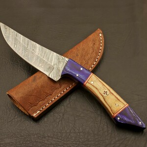 May include: A Damascus steel knife with a blue and wood handle. The knife is in a brown leather sheath.