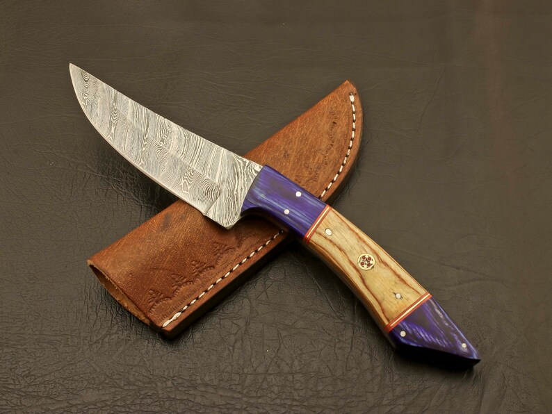 May include: A Damascus steel knife with a blue and wood handle. The knife is in a brown leather sheath.
