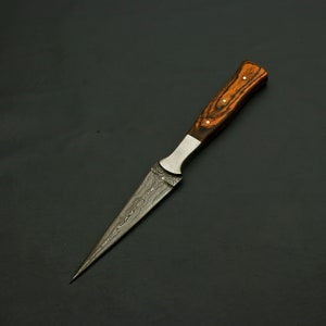 May include: A small, sharp knife with a wooden handle. The blade is made of patterned steel and has a pointed tip. The handle is made of dark wood with light brown stripes.