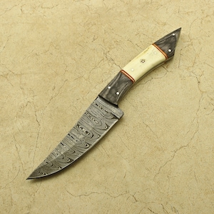 May include: A black and white Damascus steel knife with a bone handle. The handle has a copper inlay and is secured with brass pins.