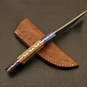 May include: A handmade knife with a blue and wood handle and a leather sheath. The blade is made of Damascus steel.