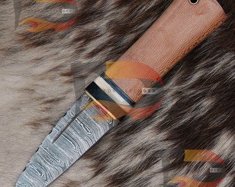 Può includere: Un coltello in acciaio Damasco con manico in legno marrone e una fascia metallica decorativa. La lama presenta un motivo ondulato e una punta affilata.