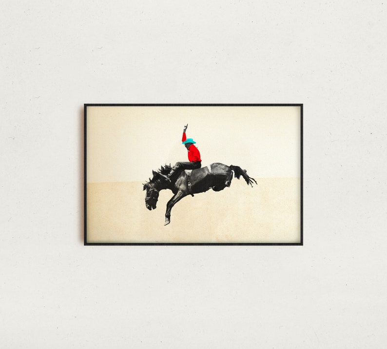 May include: A framed art print featuring a cowboy riding a bucking bronco. The cowboy is wearing a red shirt and a blue hat. The horse is black and white, and the background is a light beige color.