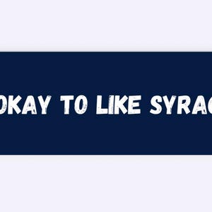 May include: A navy blue rectangular graphic with the white text "IT'S OKAY TO LIKE SYRACUSE". The text is in a bold, slightly distressed font. The design is simple and direct, suitable for apparel or accessories.