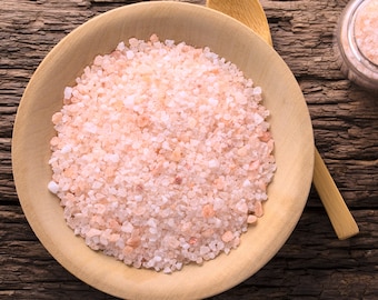 May include: A close-up of a wooden bowl filled with pink Himalayan salt crystals. The salt is a light pink color and has a coarse texture.