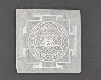 Peut inclure: Un carré de pierre gris avec un motif Sri Yantra blanc gravé à la surface. Le Sri Yantra est un symbole géométrique sacré dans l'hindouisme.