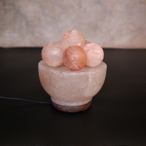 May include: A Himalayan salt lamp with a bowl-shaped base and a cluster of pink salt balls on top. The lamp is lit and glows a warm orange colour.