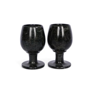 Pode incluir: Duas taças de vinho em mármore verde escuro com um padrão salpicado. As taças têm uma forma de taça arredondada, uma haste curta e uma base circular. As taças são exibidas em um fundo branco.