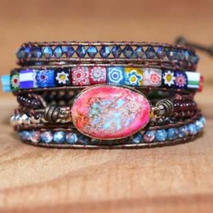 May include: Wrap bracelet featuring multiple strands of beads in blue, brown, and multicolored designs. The bracelet includes a large, oval-shaped pink and orange stone. The bracelet is wrapped with brown leather.