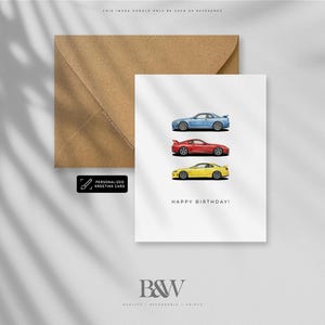 May include: A white greeting card with three illustrations of sports cars in blue, red, and yellow. The card reads "HAPPY BIRTHDAY!" in black text. A brown envelope and a "PERSONALIZED GREETING CARD" sticker are also present.