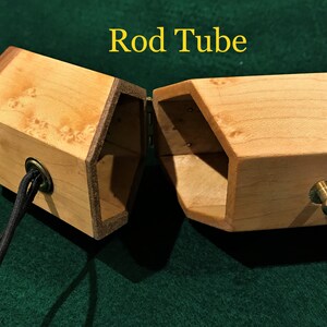 May include: A wooden rod tube with a hexagonal shape, featuring a hinged lid and a leather strap. The tube is made of light wood with a natural finish and has a brass knob on the side.