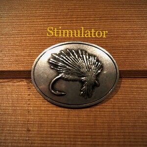 May include: A silver-toned metal pin with a detailed image of a Stimulator fly. The pin is round and has a smooth, polished finish.