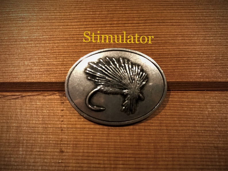 May include: A silver-toned metal pin with a detailed image of a Stimulator fly. The pin is round and has a smooth, polished finish.