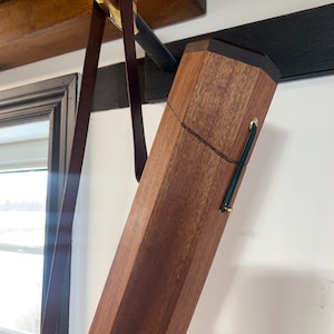 May include: A wooden case with a leather strap hanging from it. The case is made of dark wood and has a brass latch. The strap is brown leather and has a brass buckle.