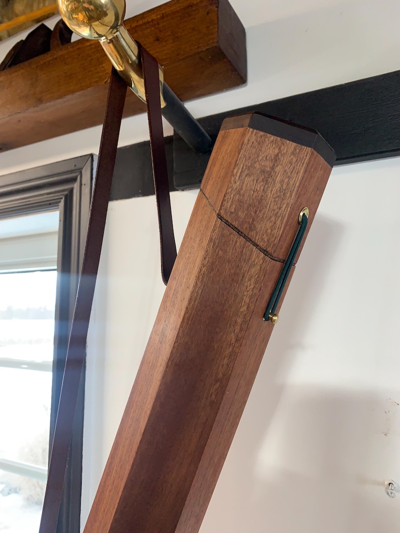 May include: A wooden case with a leather strap hanging from it. The case is made of dark wood and has a brass latch. The strap is brown leather and has a brass buckle.